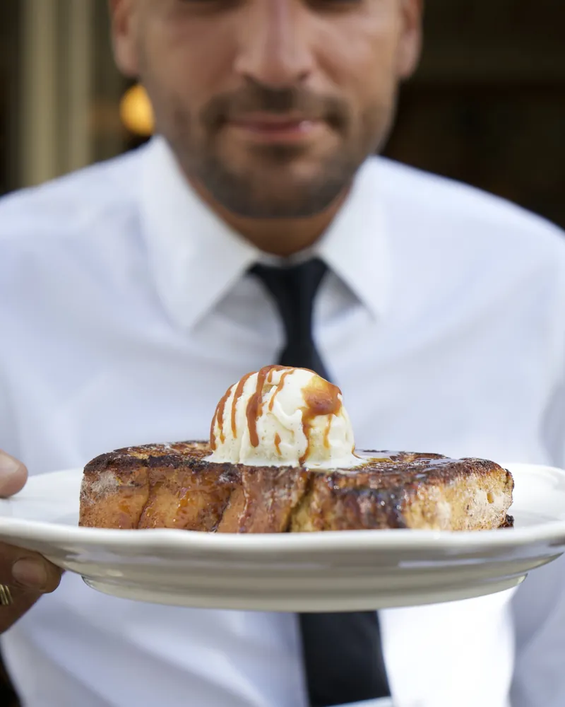 Un serveur présente un pain perdu caramélisé surmonté d'une boule de glace vanille