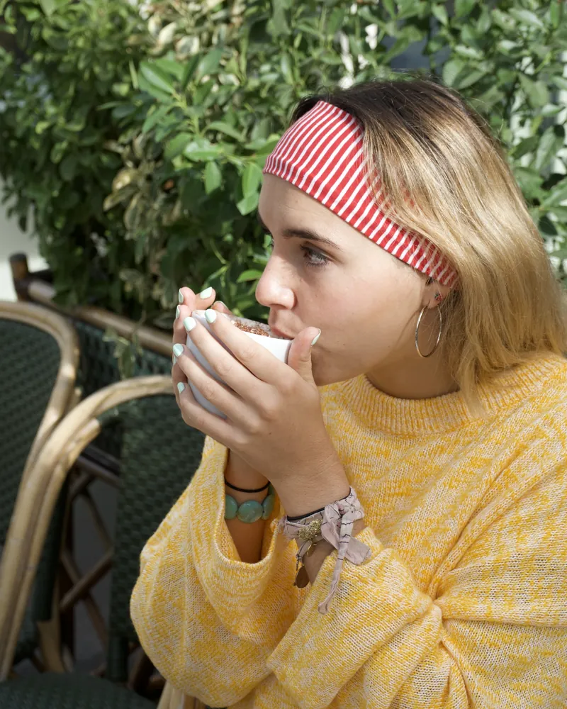 Un client en terrasse, tasse à la main, devant la verdure et les chaises en rotin