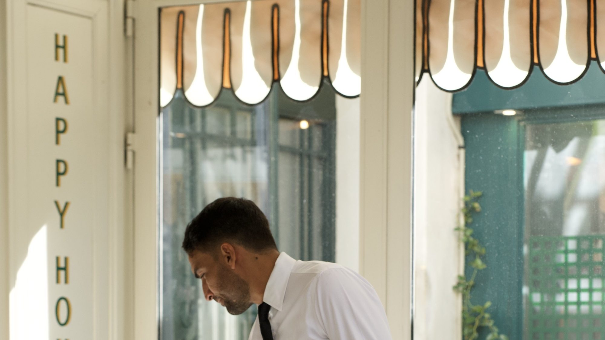 La devanture de L'Atelier Montparnasse sous son store à festons, un serveur en chemise blanche devant les baies vitrées